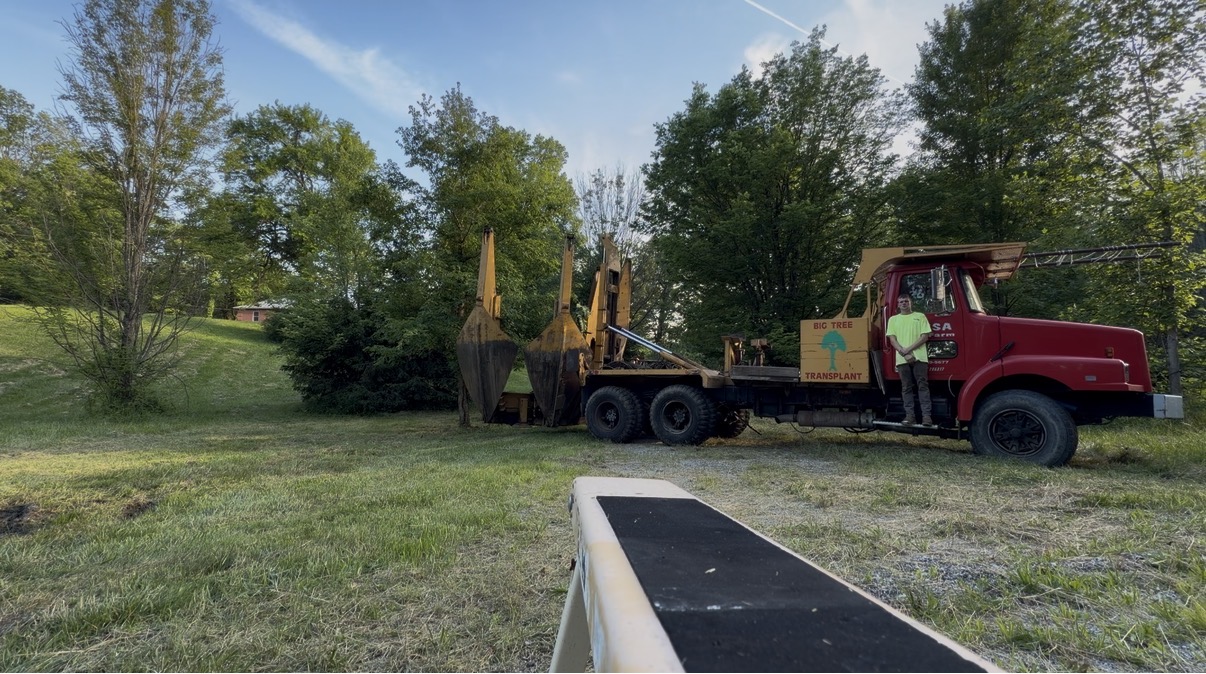 Only Trees Inc Big Tree Transplant truck with large tree spade attachment deployed, operator standing on the truck in a rural Illinois setting