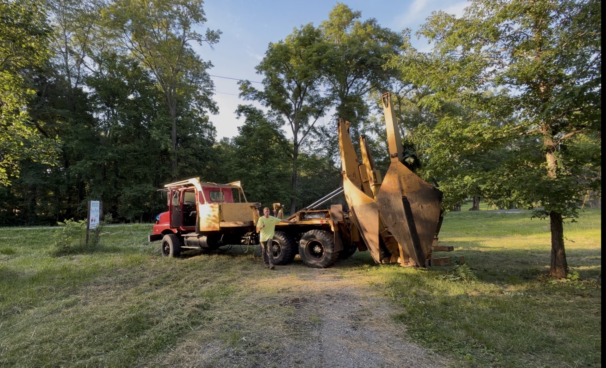 Only Trees Inc owner in green shirt standing beside the large red tree spade truck in golden hour light at a residential property